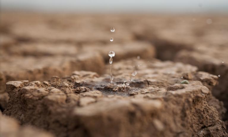 A single water droplet falling on drought-stricken soil.
