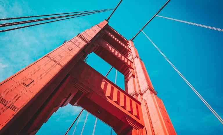View of the Golden Gate Bridge from below, showcasing its towering red structure against a bright blue sky.