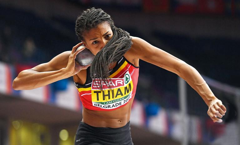 Nafi Thiam fully focused and about to throw the shot put, holding it beside her right jaw, hair partially covering her face as she prepares to throw.