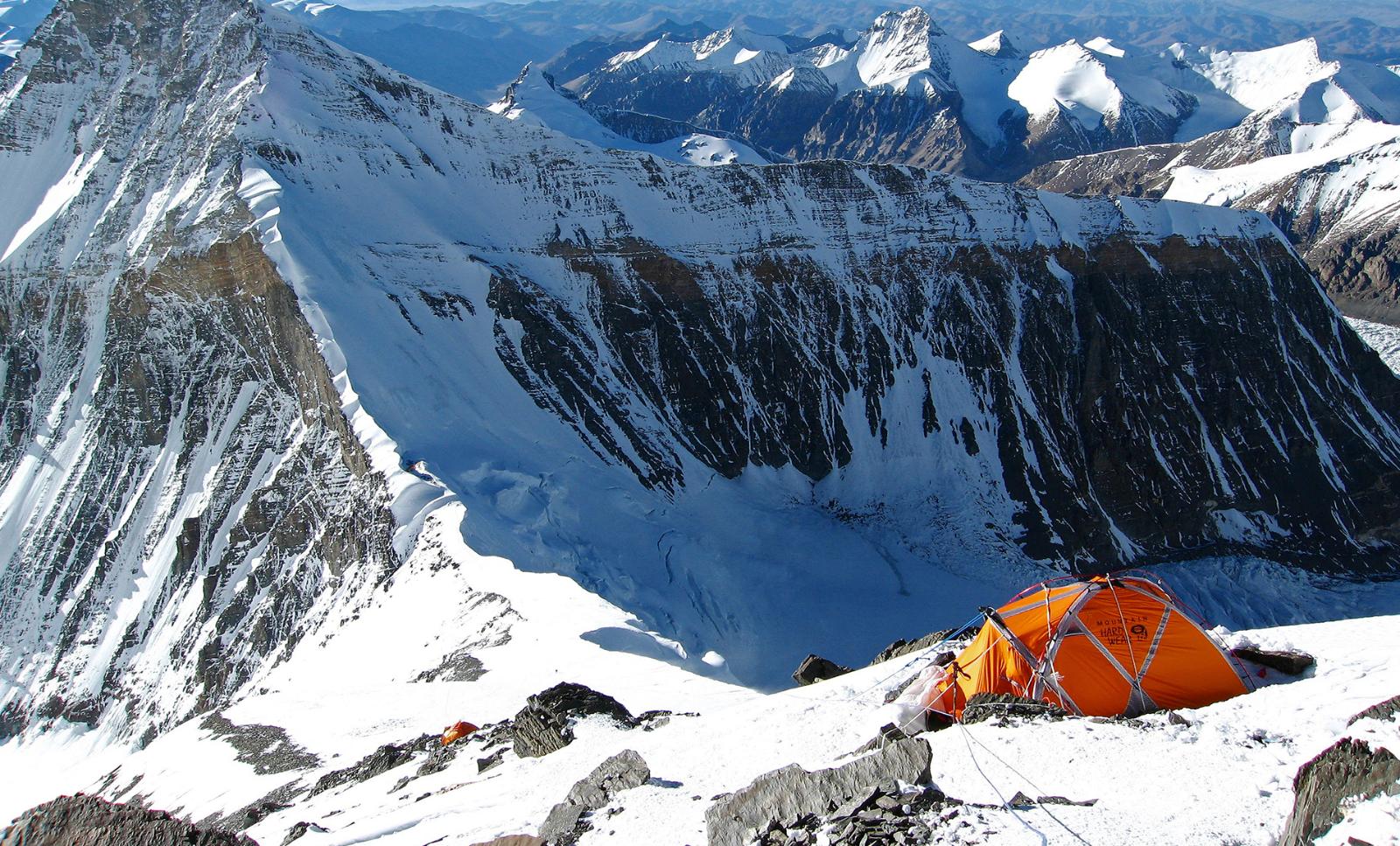 A snow-capped summit of Mount Everest and two ascending climbers, poor visibility around the summit.