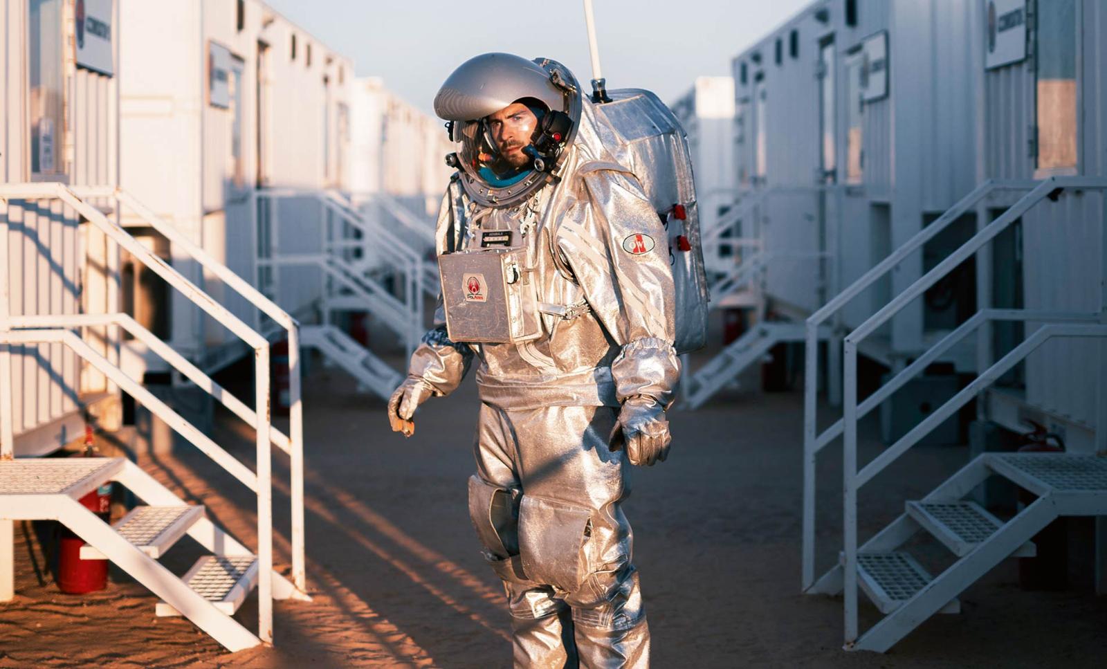 An analog astronaut stands between buildings at base camp