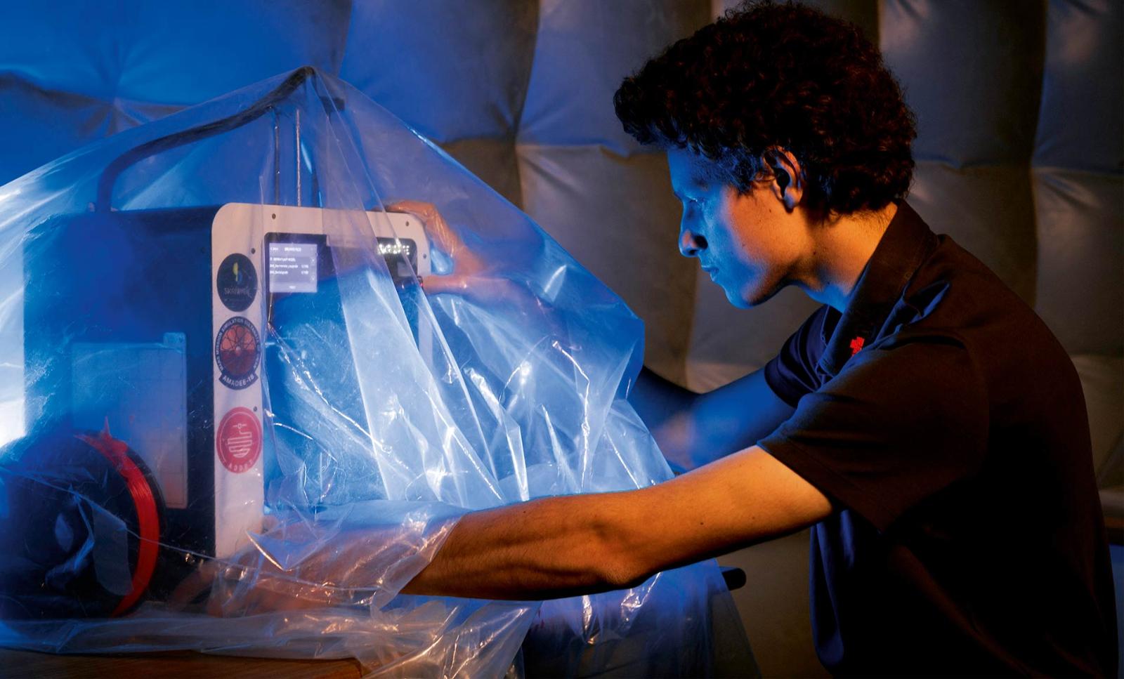 An analog astronaut works with a 3D printer