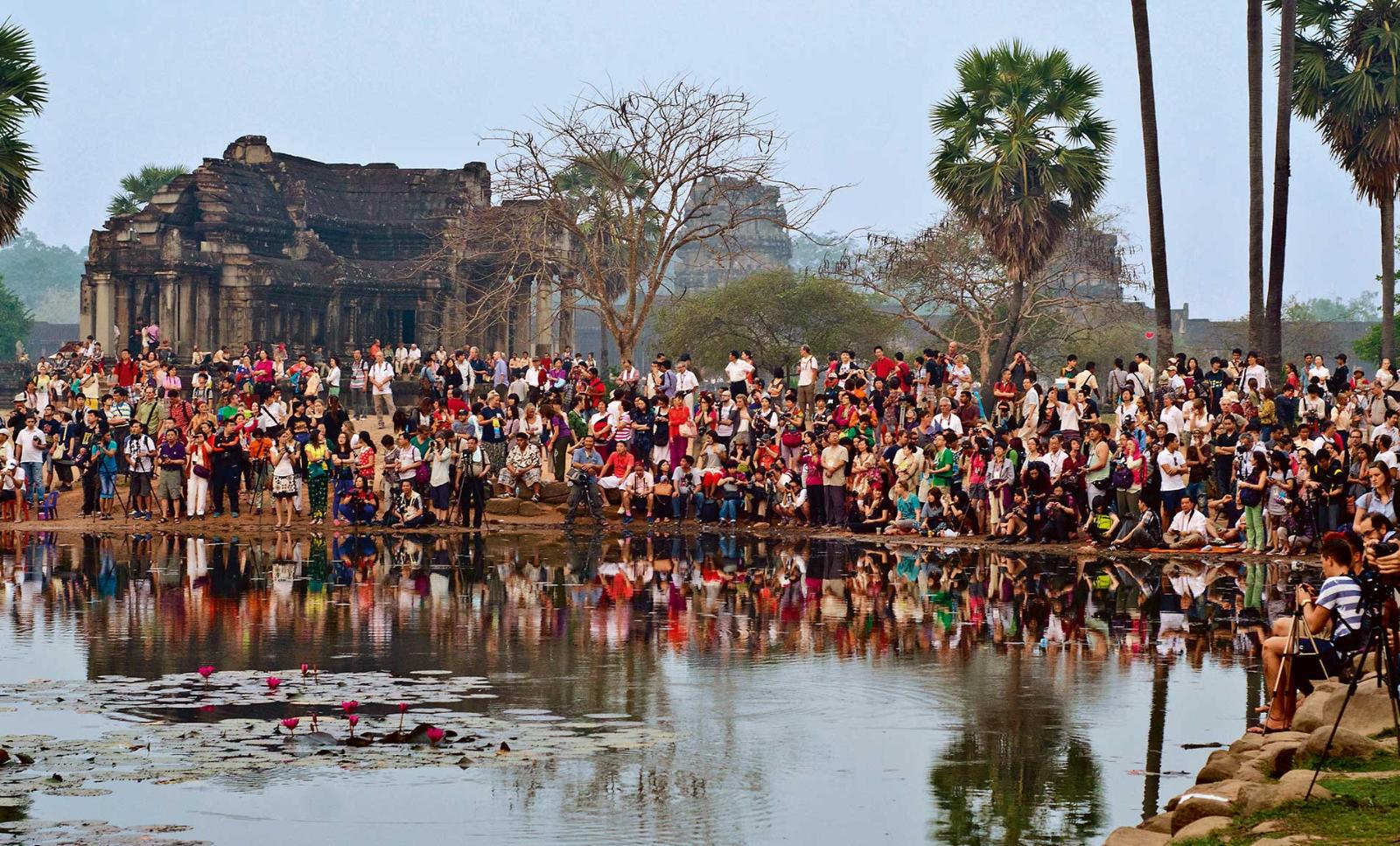 A crowd of several hundred tourists in the front of Angkor Wat temple during sunrise