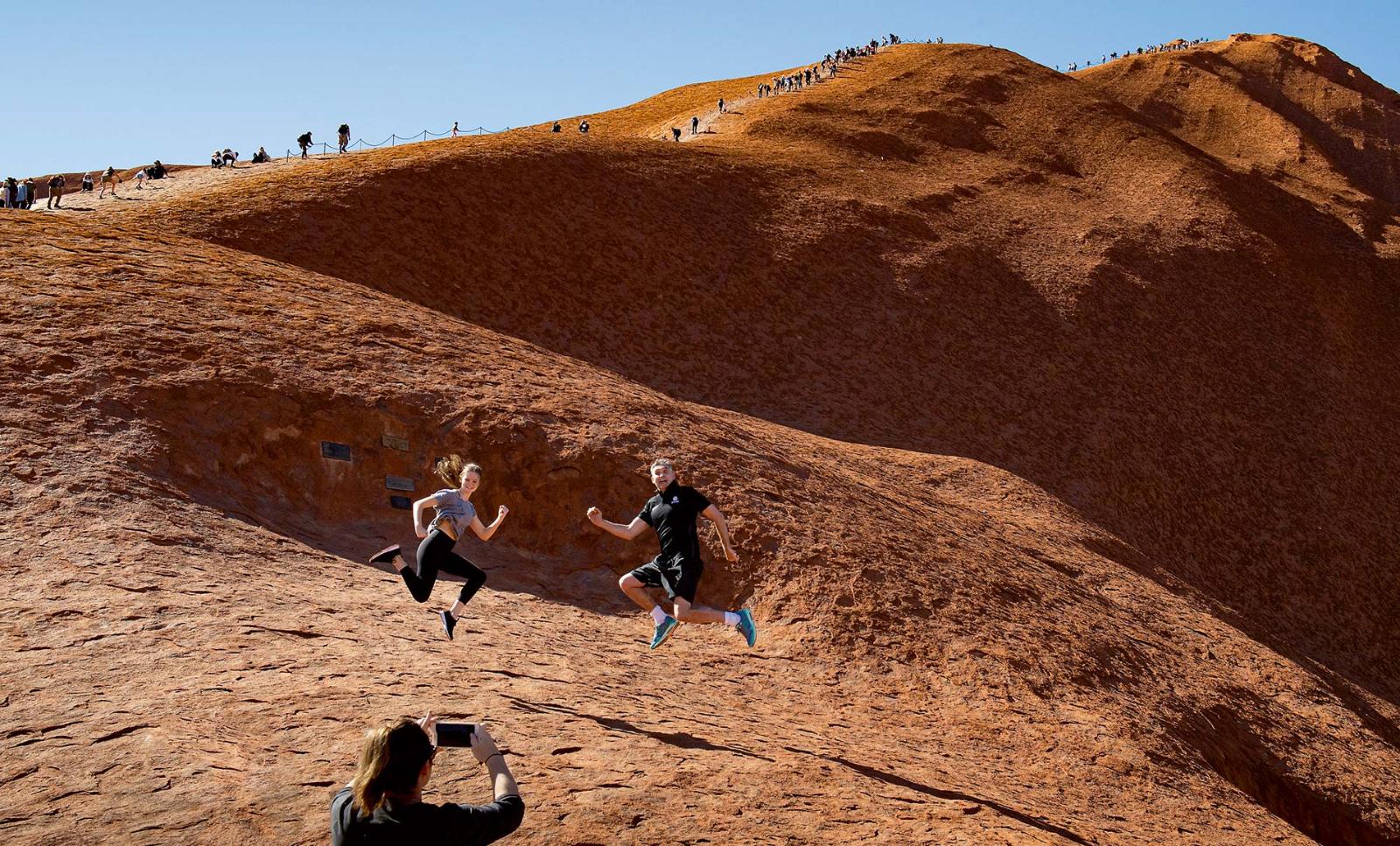 Aboriginal elders stand at the base of Uluru, also known as Ayers Rock, with a sign marking the start of a permanent climbing ban