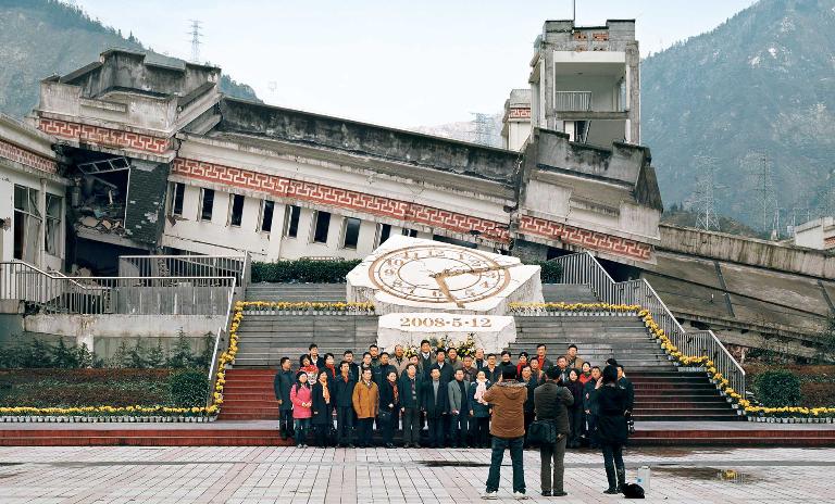 Tourists pose for a photo in front of the remains of a building destroyed in the 2008 Earthquake in China’s Wenchuan Special Tourism Zone