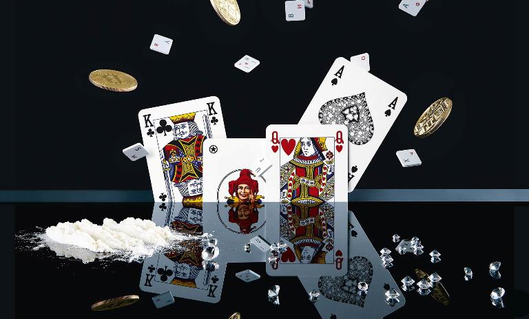 Playing cards, loose keyboard buttons and gold coins with the Bitcoin logo scatter upwards and are reflected in a high-gloss table on which a pile of white powder sits next to diamonds, symbolizing the spread of digital crime