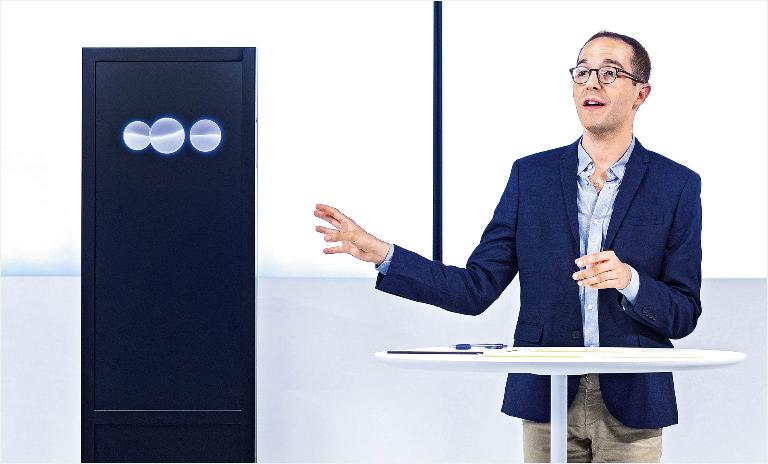 Israeli debating expert Dan Zafrir on stage next to Project Debater, and AI housed in a black box