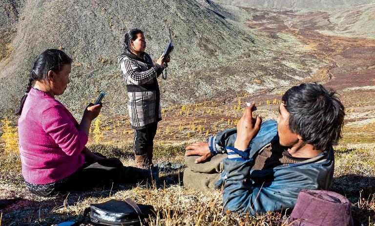 Members of the Mongolian Tsaatan reindeer shepherd tribe stand on high ground with mobile devices looking for a signal