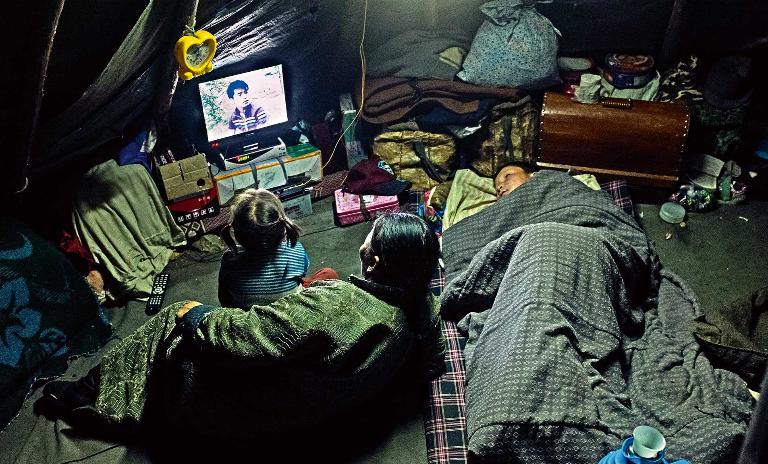 A child and two adult members of the Mongolian Tsaatan reindeer shepherd tribe watch TV inside of a teepee