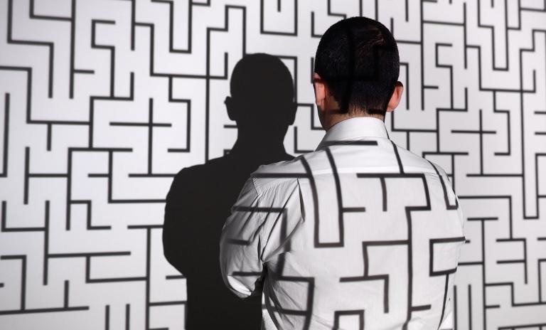 Businessman standing in front of projection screen. Projector reflects a labyrinth to screen and businessman's back.