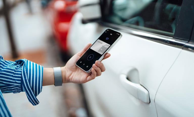 Female hand unlocking car with smart phone.