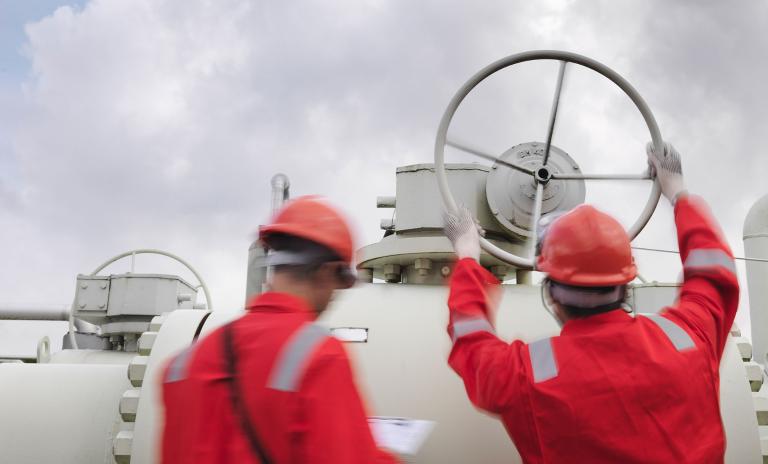 Two Men in red uniform turn a valve on the pipes.