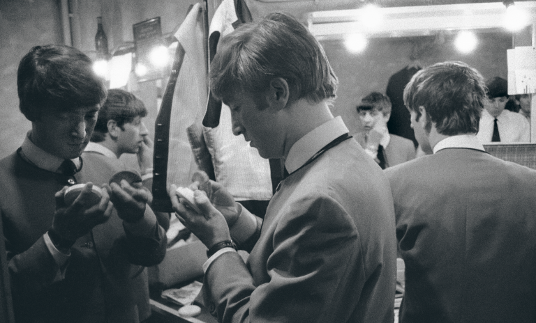 A photograph of John Lennon, Ringo Starr and Paul McCartney getting ready in a backstage mirror.