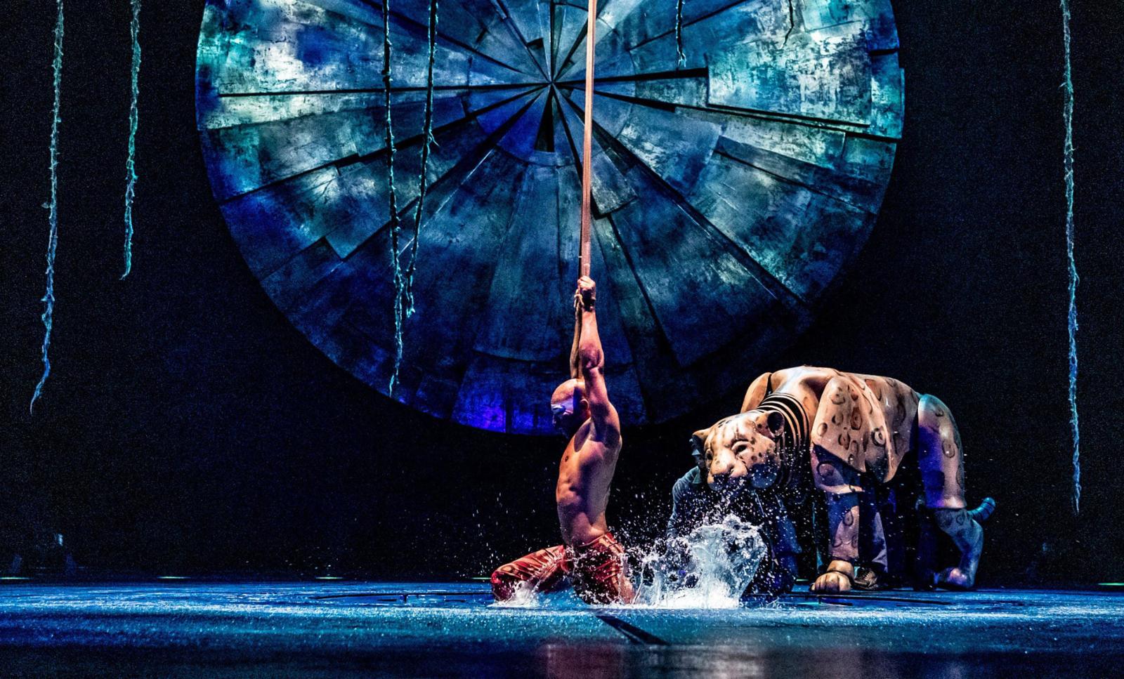 demigod of rain performs a graceful aerial straps act and interacts with a puppet resembling a life-size jaguar.
