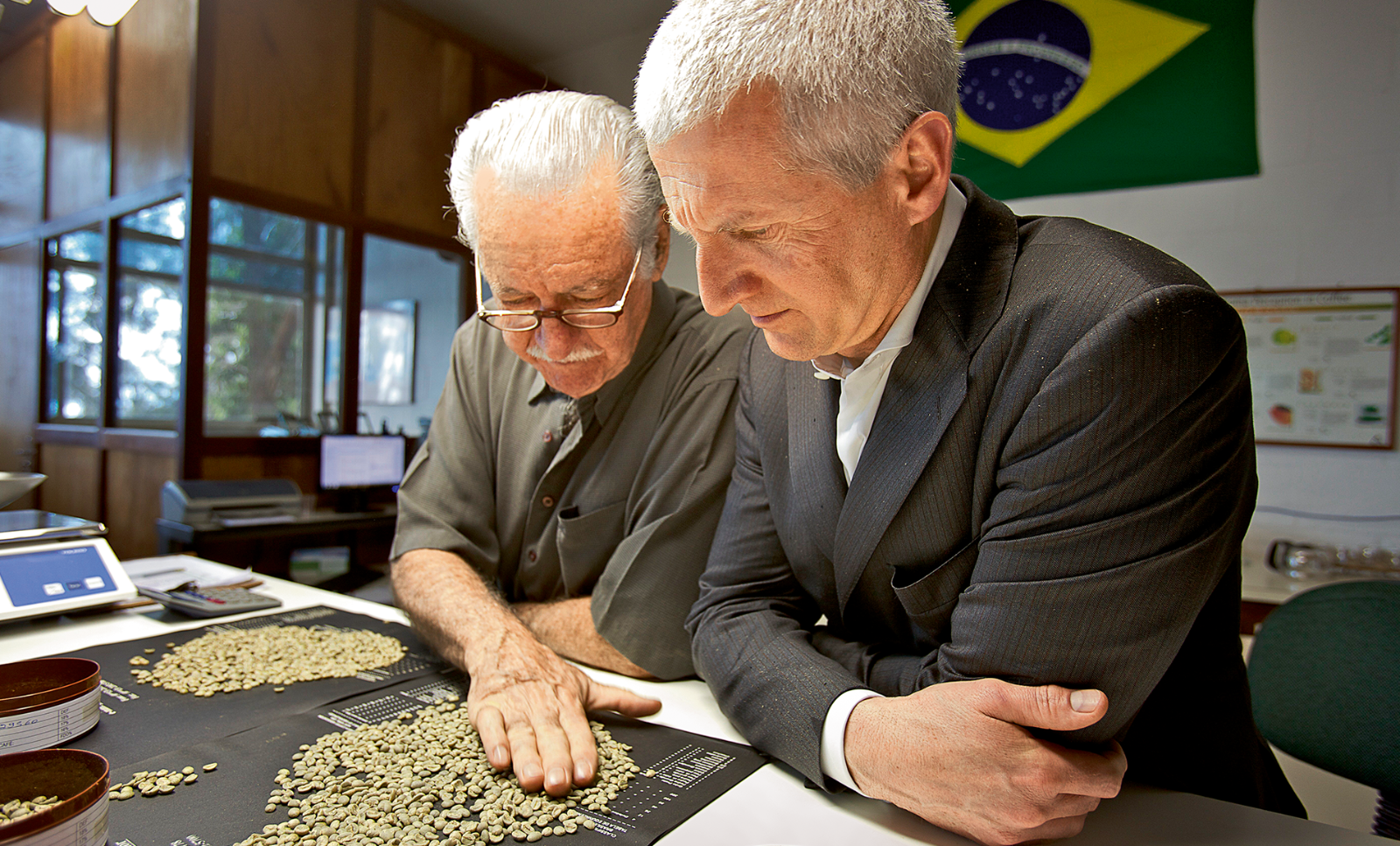 Technical advisor Aldir Teixeira inspects coffee beans with his hand. Chairman of illycaffè Andrea Illy sits next to him. (c) André Vieira/Agentur Focus