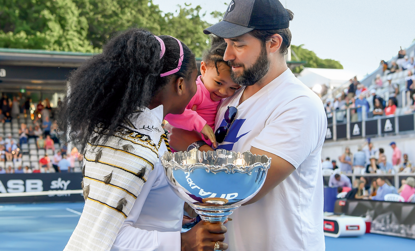 Serena Williams holding a trophy in her hand turns to her daughter Alexis Olympia and her husband Alexis Ohanian after her win against Jessica Pegula. (c) Hannah Peters/Getty Images
