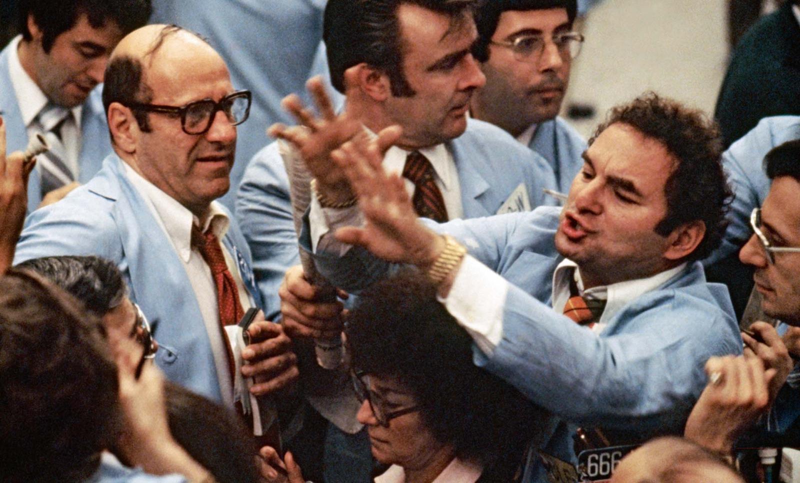 Das Foto zeigt mehrere Broker an der Börse. Einer von ihnen signalisiert mit erhobenen Händen eine Transaktion. Dabei legt er seine Arme fast auf dem Kopf der einzigen Frau im Raum ab. (c) Burt Glinn/Magnum Photos/Agentur Focus