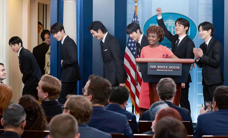 Ein Foto von der K-Pop-Gruppe BTS beim Verlassen des Presseraums im Weißen Haus. Pressesprecherin Karine Jean-Pierre steht vor ihnen auf dem Podium.