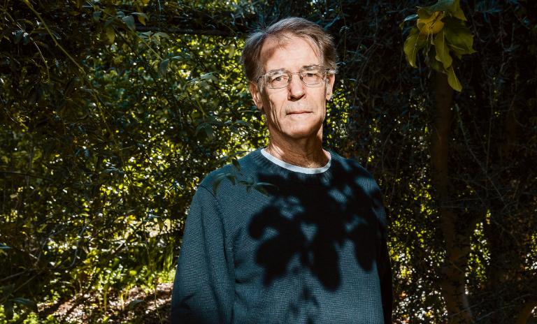 A photograph of novelist Kim Stanley Robinson surrounded by green trees.