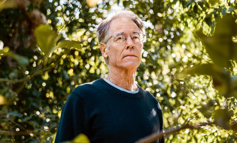A photograph of novelist Kim Stanley Robinson standing among green trees.