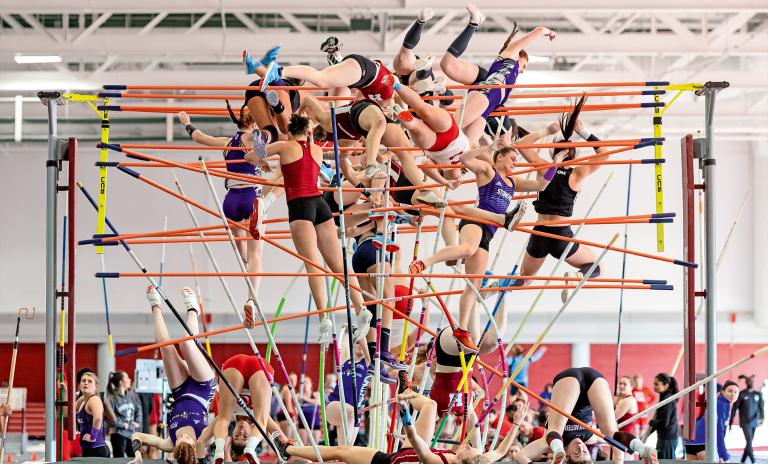 Several pole vaulters in different stages of motion appearing as if many more are competing simultaneously, some are mid-leap in the air with poles, others are in landing positions on the mat, some onlookers are at the sides.