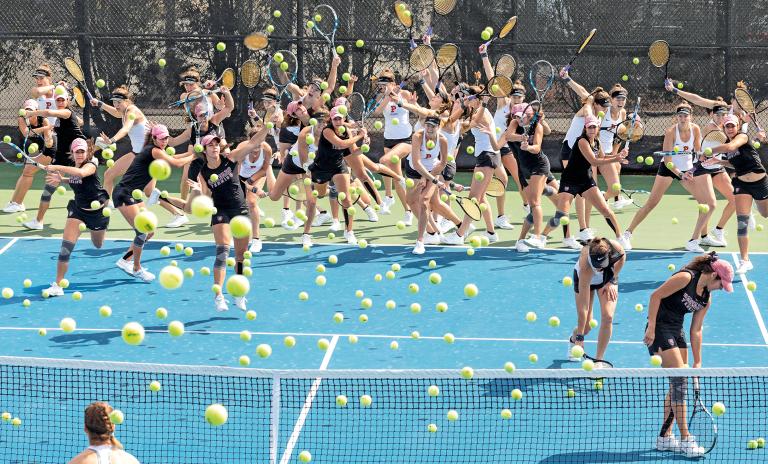 Blue tennis court; two players in different stages of motion appearing as over 30 players in the shot. Rackets and lots of tennis balls in the air at different heights.