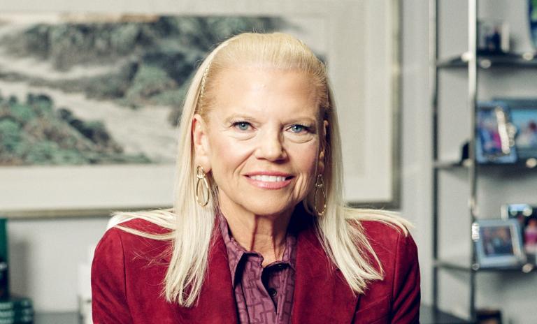 Porträtfoto von Ginni Rometty. Sie lächelt und schaut in die Kamera, hinter ihr sieht man Büroregale und ein Bild.