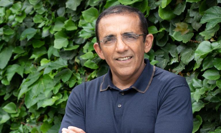 Portrait photo of Ranjay Gulati, arms folded and looking into the camera, against a backdrop of a green hedge.