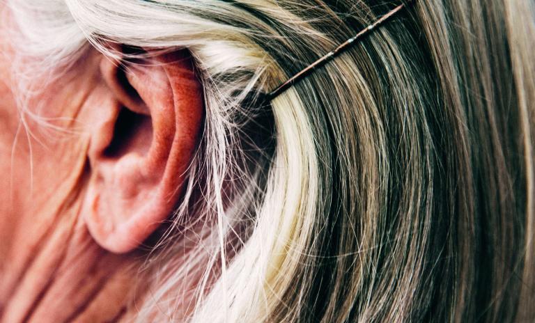 Close-up of a woman’s head, straight collarbone-length hair clipped back over her right ear with a hair grip.