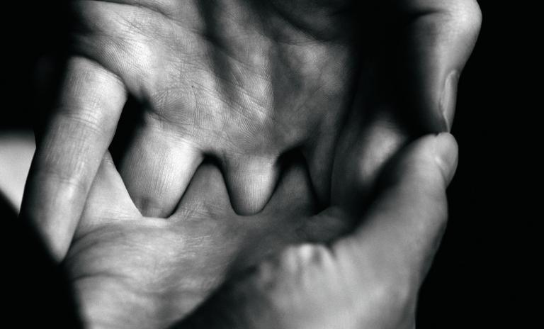 Black-and-white closeup of hands with fingers linked, dark background.