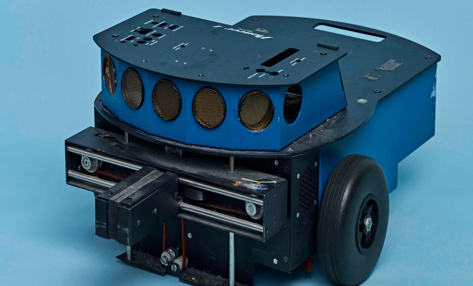 A close-up image of an early prototype of a robot against a bright blue background.