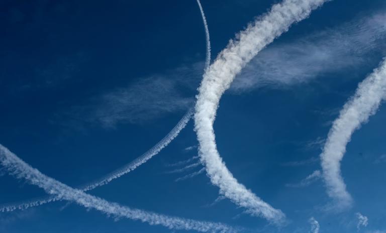 White airplane contrails in swirls against a bright blue sky.