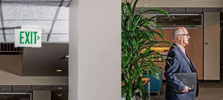 Organizational behavior expert Jeffrey Pfeffer photographed from the side as he walks underneath an “exit” sign